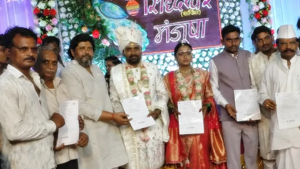 Groom Siddheshwar Pethkar and his bride standing on the wedding stage holding official group insurance policy documents for villagers.